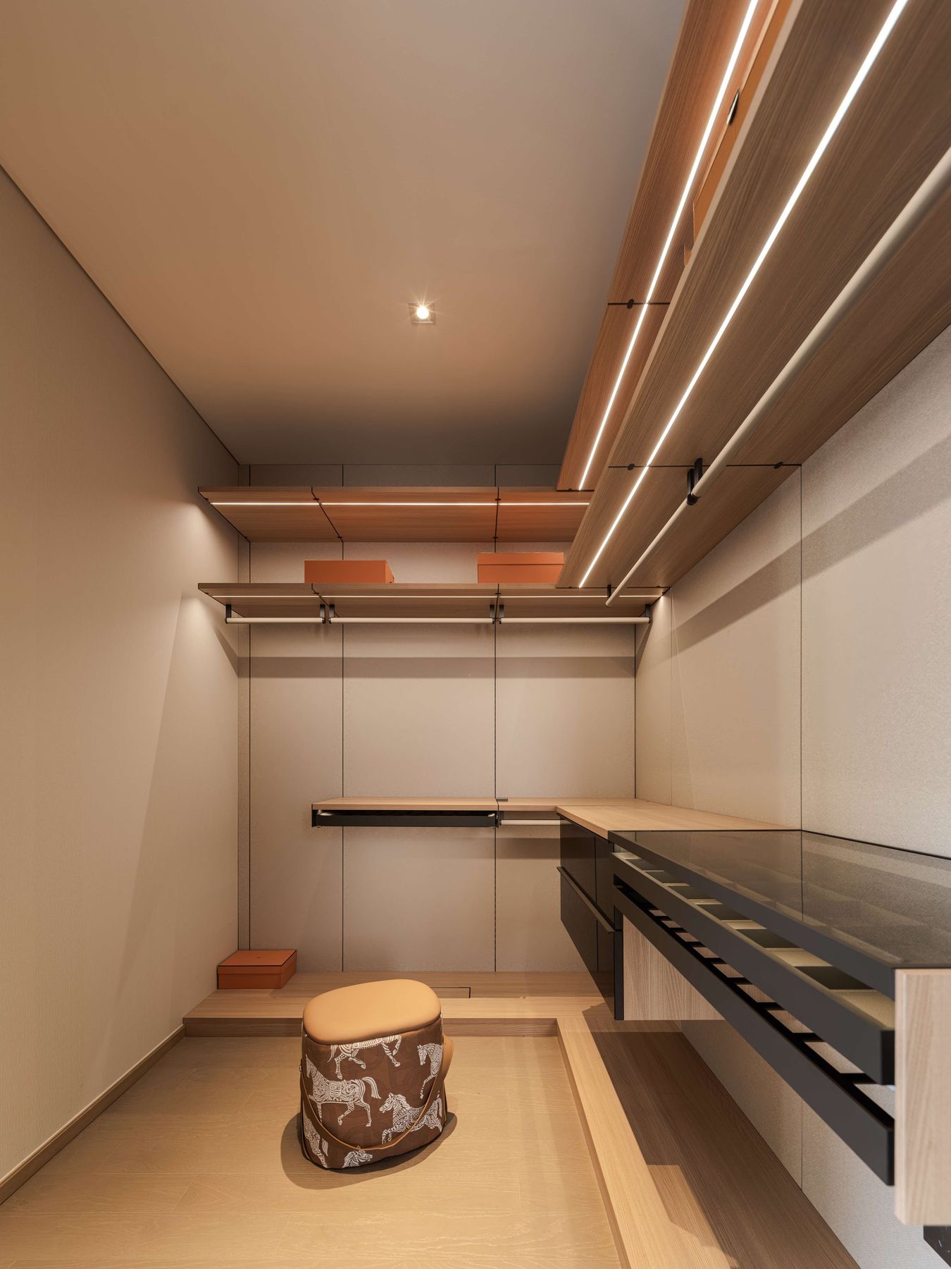 Open walk-in wardrobe with lit timber shelves and glass-top jewellery drawers