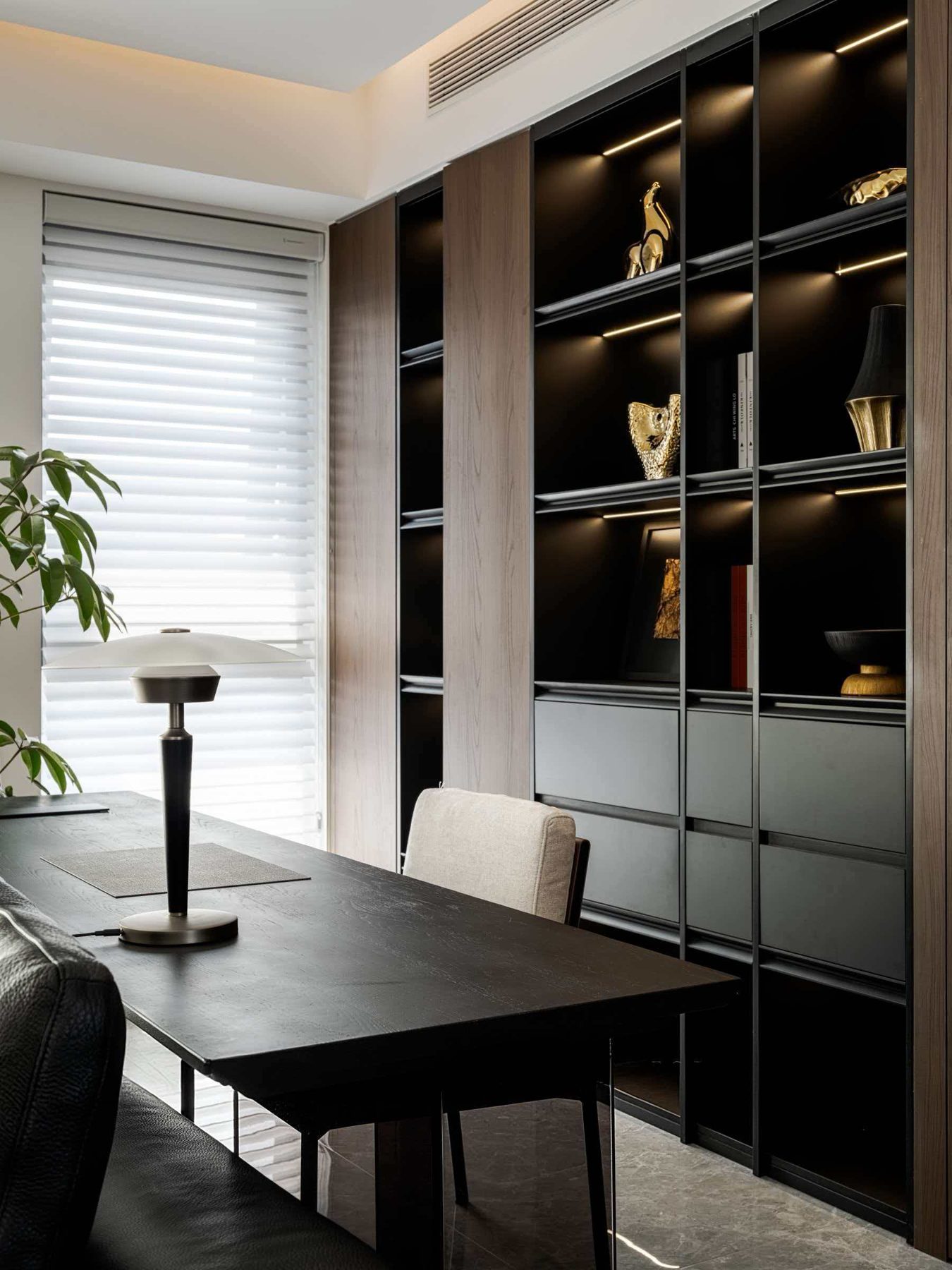 Black-framed display cabinet with lit shelves beside a desk