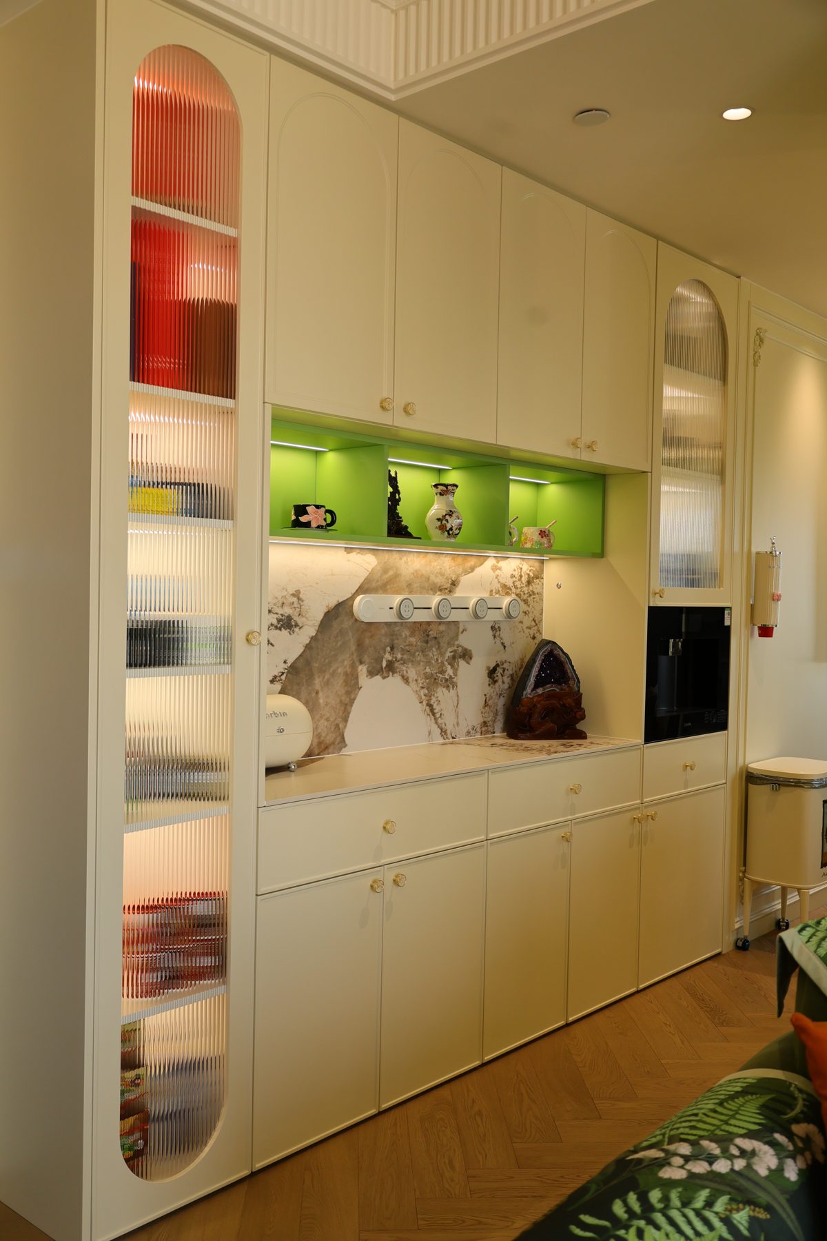 Cream cabinetry with arched glass display cabinets and a lit green niche